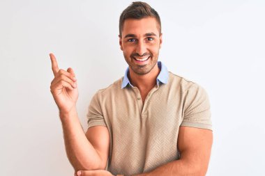 Soyutlanmış arka plan üzerinde zarif tişörtler giyen genç yakışıklı bir adam. Yüzünde kocaman bir gülümseme, eli ve parmağı kameraya bakıyor..