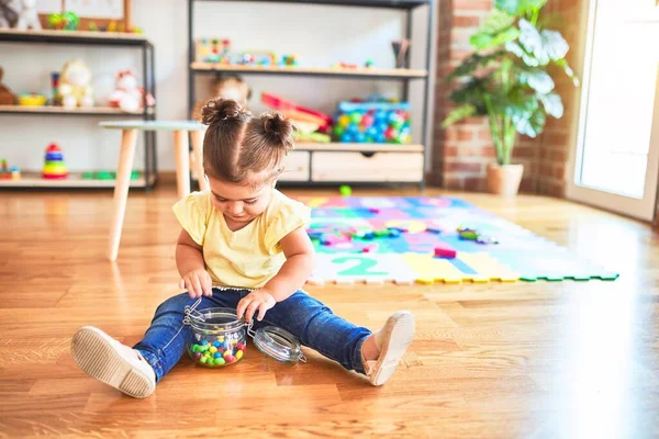 美しい幼児は幼稚園でチョコレート色のボールの瓶で床に座っています — ストック写真