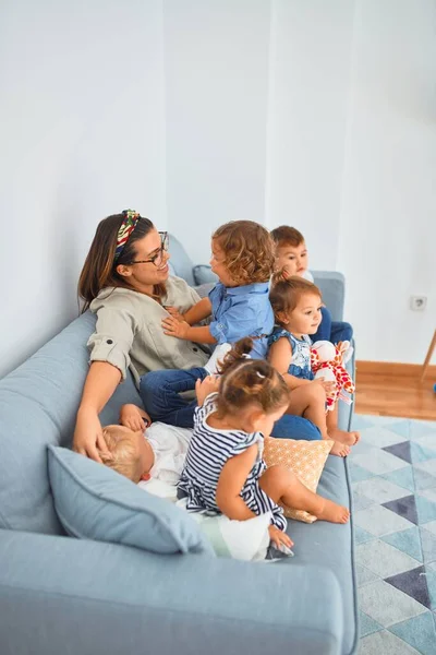Beautiful teacher and group of toddlers sitting on the sofa playing at kindergarten — Stock Image Beautiful Teacher Group Toddlers Sitting Sofa Playing Kindergarten Stock Picture