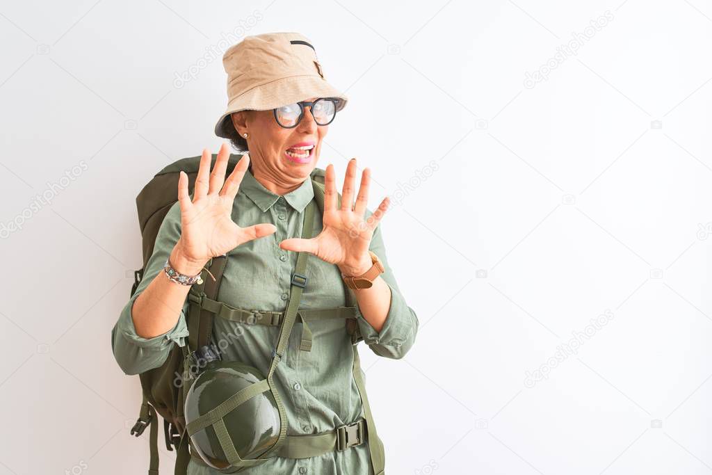 Middle age hiker woman wearing backpack canteen hat glasses over isolated white background afraid and terrified with fear expression stop gesture with hands, shouting in shock. Panic concept.