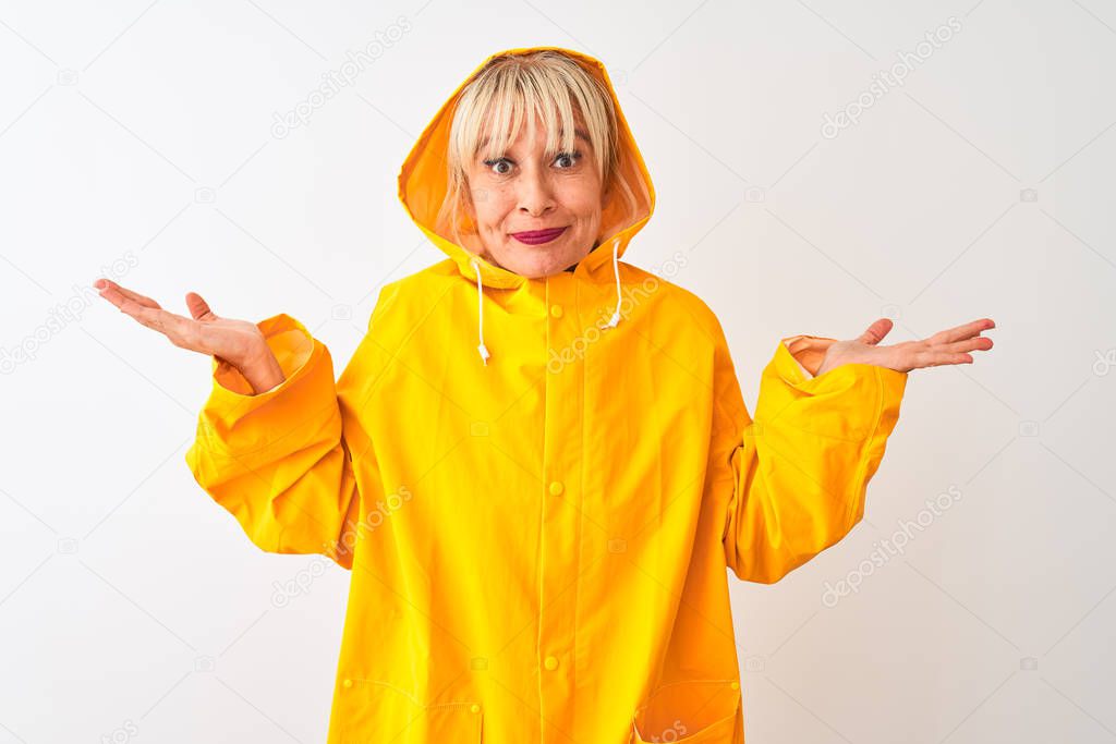 Middle age woman wearing rain coat with hood standing over isolated white background clueless and confused expression with arms and hands raised. Doubt concept.