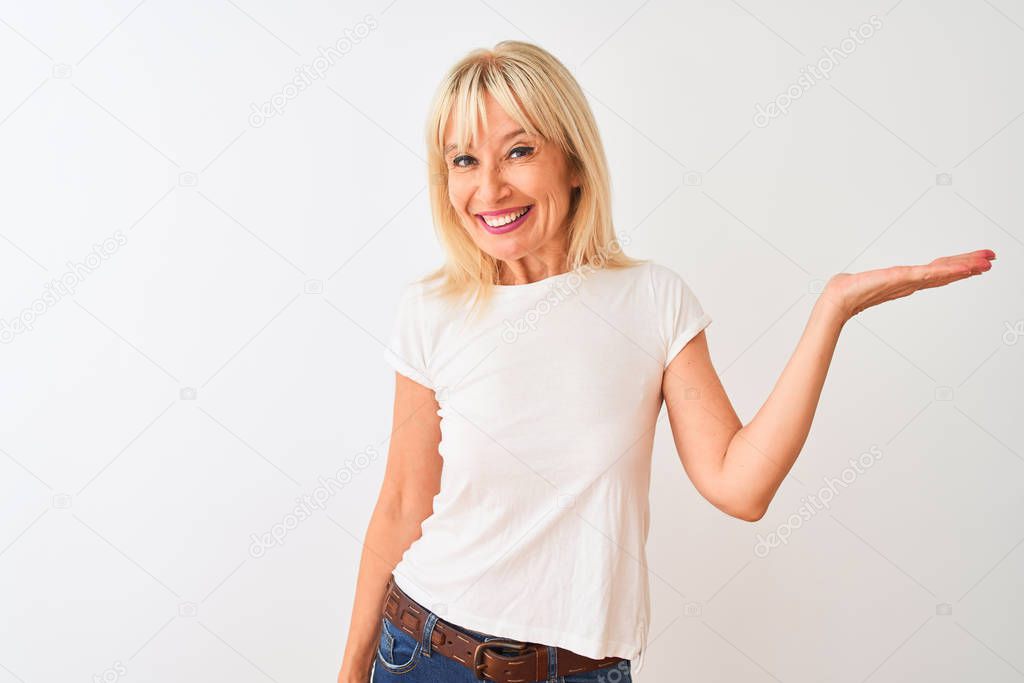 Middle age woman wearing casual t-shirt standing over isolated white background smiling cheerful presenting and pointing with palm of hand looking at the camera.