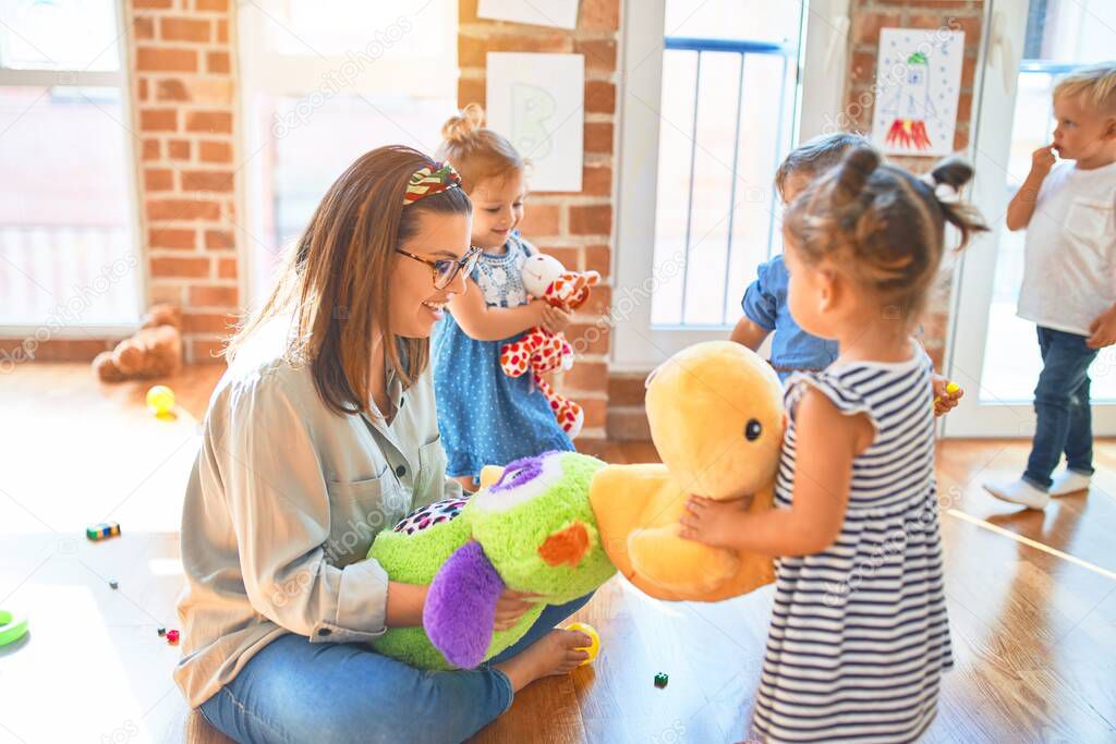 Beautiful teacher and group of toddlers playing around lots of toys at kindergarten