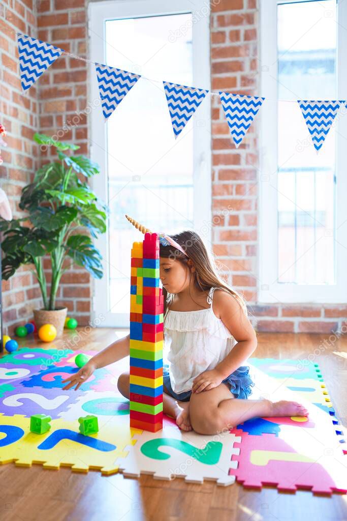 Adorable toddler playing with building blocks toy around lots of toys at kindergarten