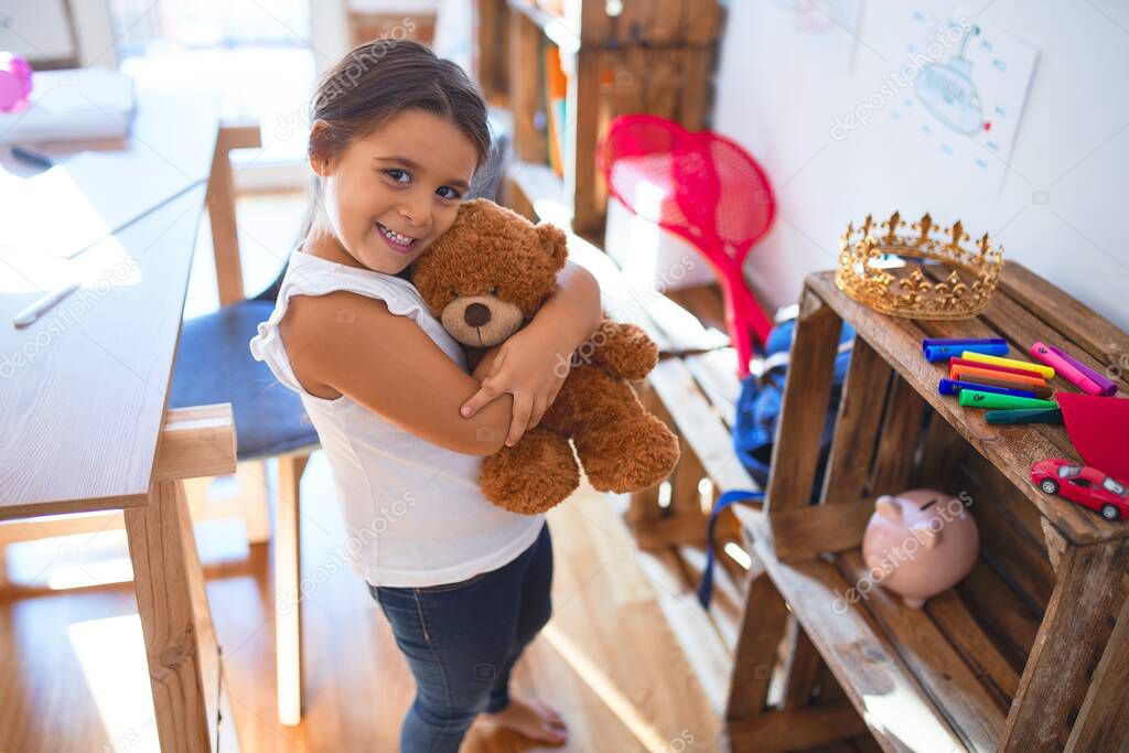 Adorable toddler smiling happy hugging teddy bear around lots of toys at kindergarten