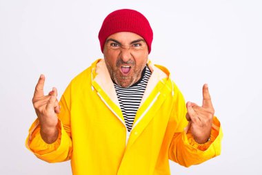 Yağmurluk giyen ve yünlü şapka takan orta yaşlı bir adam izole edilmiş beyaz arka planda duruyor çılgın bir ifadeyle elleri havada rock sembolü yapıyor. Müzik yıldızı. Ağır konsept.