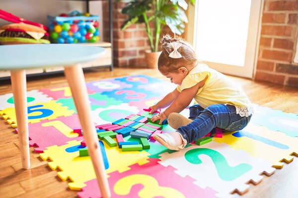 Красивый ребенок сидит на ковре-головоломке, играя с деревянными кирпичами в детском саду
