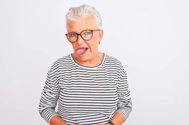 İzole edilmiş beyaz arka plan üzerine çizgili donanma tişörtü gözlüğü takan yaşlı gri saçlı kadın komik bir ifadeyle dilini dışarı çıkarıyor. Duygu kavramı.