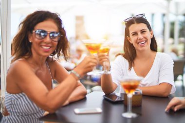 Güzel anne ve kızı restoranın terasında oturmuş kokteyl içiyor ve gülümsüyor.