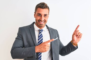 Takım elbiseli ve kravatlı genç yakışıklı iş adamı izole edilmiş arka planda gülümsüyor ve kameraya bakıyor iki eliyle ve parmaklarıyla kenarı işaret ediyor..