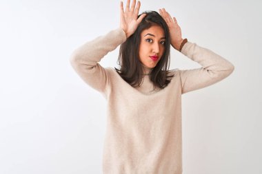 Beautiful chinese woman wearing turtleneck sweater standing over isolated white background Doing bunny ears gesture with hands palms looking cynical and skeptical. Easter rabbit concept.