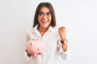 Gözlüklü güzel bir iş kadını, kumbarasını soyutlanmış beyaz arka planda tutuyor gururla bağırıyor, zaferi ve başarıyı kutluyor çok heyecanlı, coşkulu bir duygu.