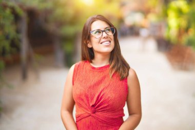 Genç ve güzel bir kız gülümseyerek mutlu ve kendinden emin bir şekilde parkta yürüyor, yüzünde bir gülümsemeyle duruyor.