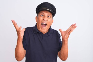 Senior grey-haired man wearing black polo and captain hat over isolated white background crazy and mad shouting and yelling with aggressive expression and arms raised. Frustration concept.