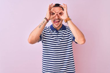 Genç yakışıklı adam pembe izole edilmiş arka plan üzerinde deniz çizgili tişört giyiyor. Dürbün gibi güzel bir jest yapıyor. Gözleri parmaklarından bakıyor. Çılgın ifade.