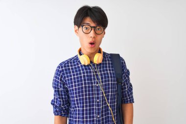 Sırt çantası ve kulaklık takan Çinli bir öğrenci beyaz arka plan üzerinde korku, korku ve heyecan dolu bir yüz ifadesiyle dehşete düşmüş ve şok olmuştu..