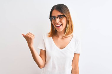 Güzel kızıl saçlı, gözlüklü, izole edilmiş arka planda gülümseyen, gülümseyen ve başparmağıyla yan tarafı gösteren bir kadın..