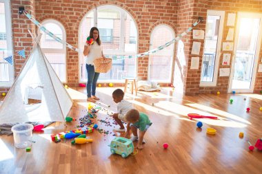 Anaokulunda bir sürü oyuncağın etrafında basketbol oynayan genç ve güzel öğretmenler ve yeni yürümeye başlayan çocuklar.