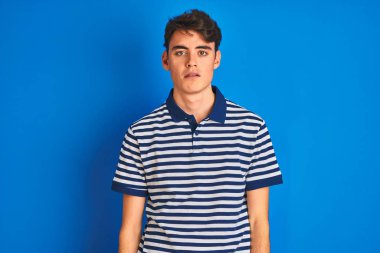 Teenager boy wearing casual t-shirt standing over blue isolated background looking sleepy and tired, exhausted for fatigue and hangover, lazy eyes in the morning.