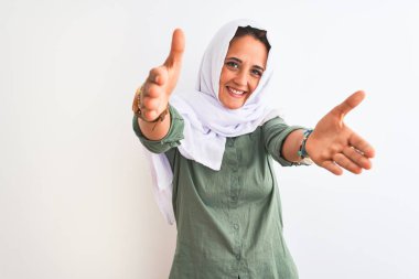 Geleneksel Müslüman tesettürlü genç, güzel bir Arap kadın izole edilmiş arka planda kameraya sarılmak için kollarını açıp gülümseyerek bakıyor. Mutluluğu kucaklayan neşeli bir ifade..