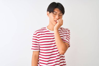 Gözlüklü ve çizgili tişörtlü genç Çinli adam izole edilmiş beyaz arka planda duruyor. Elleri ağızdan tırnak yerken gergin ve stresli görünüyor. Endişe sorunu.