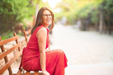 Mutlu ve kendinden emin gülümseyen genç bir kız. Kasaba parkında oturuyor. Yüzünde bir gülümsemeyle.