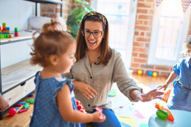 Güzel öğretmen ve bir grup çocuk anaokulunda bir sürü oyuncakla oynuyorlar.
