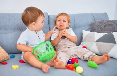 Güzel bebekler, biri ağlıyor, kanepede oturuyor, evde oyuncaklarla oynuyor.