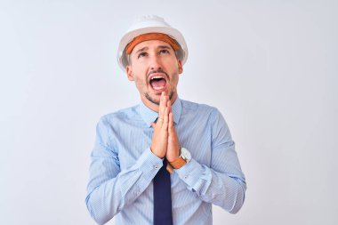 Müteahhit kaskı takan genç bir iş adamı, izole edilmiş arka planda yalvarıyor ve dua ediyor. Yüzünde umut ifadesi var. Çok duygusal ve endişeli. Af diliyor. Din kavramı.