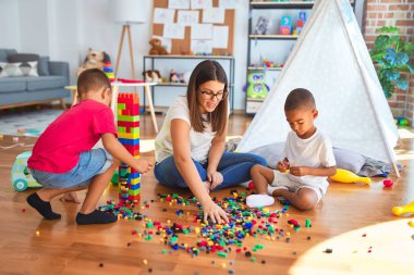 Anaokulundaki bir sürü oyuncağın etrafına taş döşeyen genç ve güzel öğretmenler ve yeni yürümeye başlayan çocuklar.