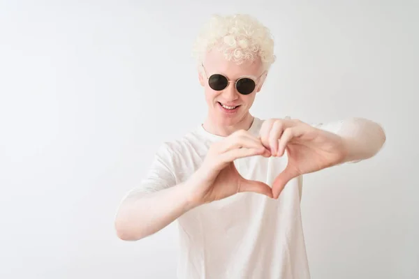 年轻的白化病金发男人穿着T恤 戴着太阳镜 站在孤独的白色背景上 带着爱的笑容 用手表现出心脏的象征和形体 浪漫的概念 — 图库照片