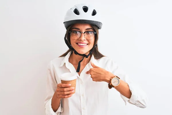 Beautiful businesswoman wearing bike helmet drinking coffee over isolated white background with surprise face pointing finger to himself