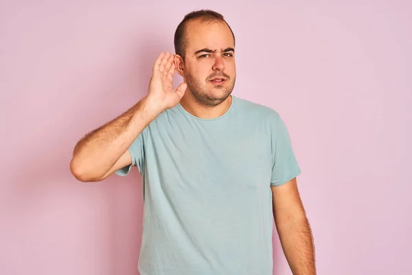 青いカジュアルなTシャツを着た若い男が 噂やゴシップに耳を傾けながら手で笑って孤立したピンクの背景の上に立っている 病気の概念 — ストック写真