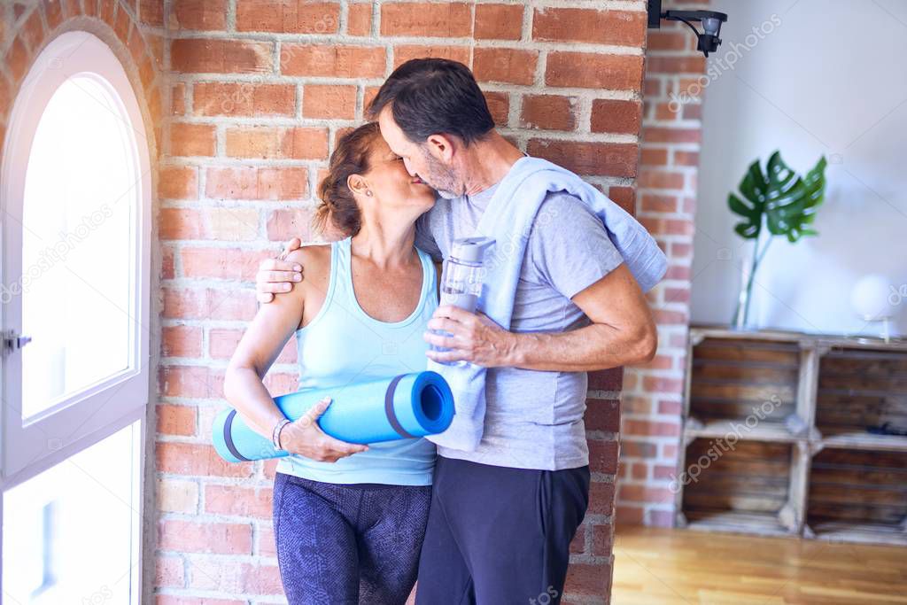 Middle age beautiful sporty couple standing hugging and kissing at gym
