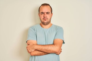 Young man wearing blue casual t-shirt standing over isolated white background skeptic and nervous, disapproving expression on face with crossed arms. Negative person.