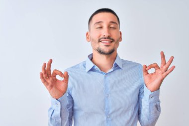 Tecrit edilmiş arka planda duran genç yakışıklı iş adamı rahatla ve gözün kapalı gülümse parmaklarınla meditasyon hareketi yap. Yoga konsepti.
