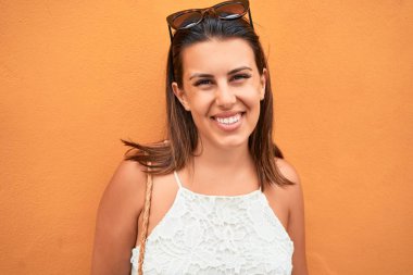 Turuncu duvara yaslanan güzel kız, güneşli bir yaz gününde gülümseyen genç arkadaş.