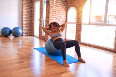 Orta yaşlı güzel sporcu kadın mutlu gülümsüyor. Spor salonunda yoga sınıfında spor topu kullanarak egzersiz yapmak.