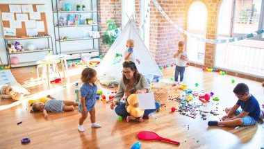 Güzel öğretmen ve bir grup çocuk anaokulunda bir sürü oyuncakla oynuyorlar.