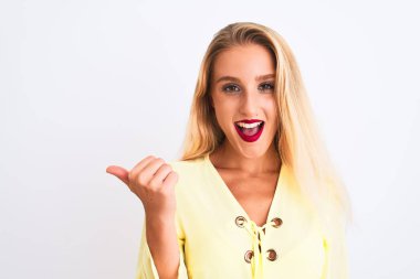 Zarif sarı tişört giyen genç ve güzel bir kadın izole edilmiş beyaz arka planda dikiliyor ve baş parmağıyla gülümseyerek yüzünü gösteriyor.