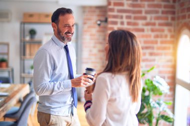 Two middle age business workers smiling happy and confident. Standing with smile on face working together holding glass of coffee at the office clipart