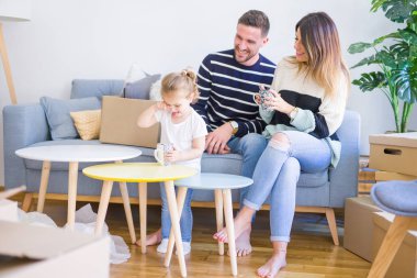 Güzel aile, anne-babalar kanepede kahve içme oturmuş karton kutular etrafında yeni evde oynayan çocuğuna bakıyor