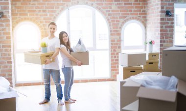 Young beautiful couple sitting on the floor at new home around cardboard boxes celebrating surprised and amazed for success with arms raised and open eyes. Winner concept.