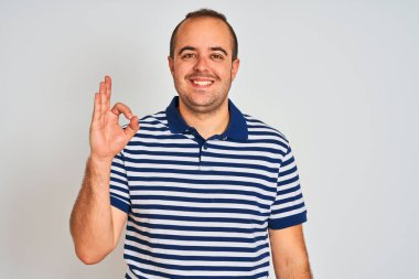 Young man wearing casual striped polo standing over isolated white background smiling positive doing ok sign with hand and fingers. Successful expression.