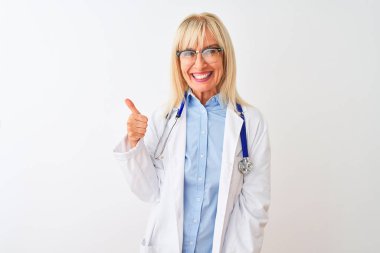 Gözlüklü ve steteskop takan orta yaşlı bir kadın izole edilmiş beyaz arka planda mutlu bir el hareketi yapıyor. Kameraya bakıp başarıyı gösteren ifade onaylanıyor.