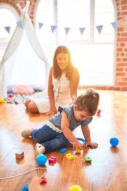 Genç, güzel öğretmen ve bebek yerde oturmuş anaokulundaki oyuncak trenlerle oynuyorlar.