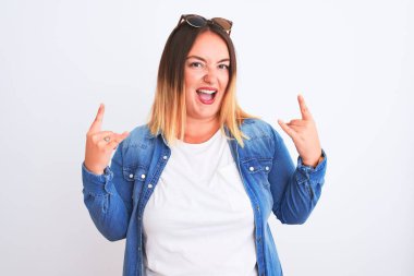 İzole edilmiş beyaz arka planda duran kot gömlekli güzel bir kadın çılgın bir ifadeyle el kaldırarak rock sembolü yapıyor. Müzik yıldızı. Ağır müzik konsepti.