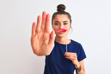 Güzel bir kadın, popo partisi bıyığını izole edilmiş beyaz arka plan üzerinde tutuyor. Açık elle dur işareti yapıyor. Ciddi ve kendinden emin bir ifadeyle, savunma jesti.