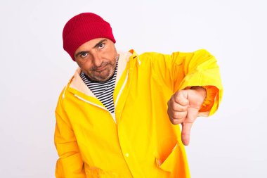 Yağmurluk ve yünlü şapka giyen orta yaşlı bir adam, izole edilmiş beyaz arka planda dikiliyor mutsuz ve kızgın görünüyor, reddedilmiş ve olumsuz hareketler yapıyor. Kötü ifade.