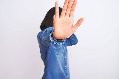 Young beautiful chinese woman wearing denim shirt standing over isolated white background covering eyes with hands and doing stop gesture with sad and fear expression. Embarrassed and negative concept.